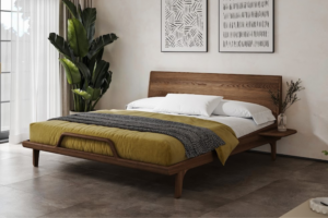 Moderní postel z masivního jasanu v elegantním odstínu ořechu s vysokým čelem, stylovým dřevěným rámem a originálním designovým detailem v přední části. Jemné křivky a vzdušná konstrukce vytvářejí harmonický kus nábytku s nadčasovým designem.